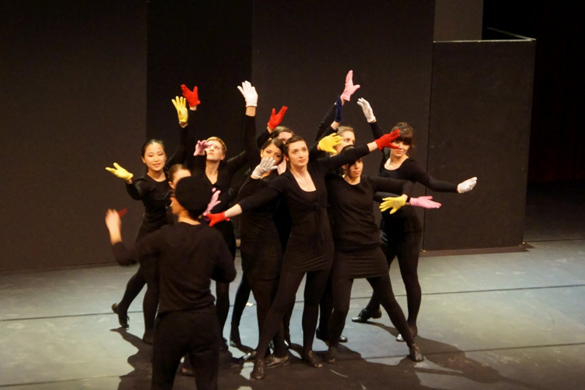 Women on stage in black clothing with colorful gloves