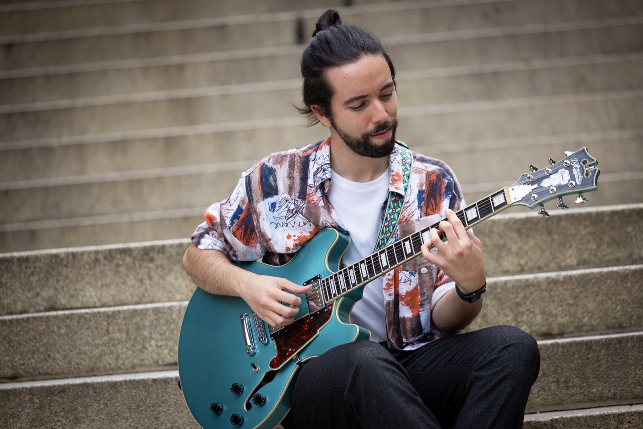 Mann sitzt mit E-Gitarre auf einer grauen Steintreppe und spielt
