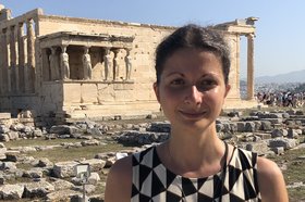 Portrait einer dunkelhaarigen Frau vor einem antiken Bauwerk im Hintergrund