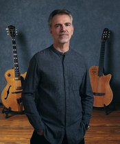 Porträt von Roland Cabezas mit zwei Gitarren im Hintergrund