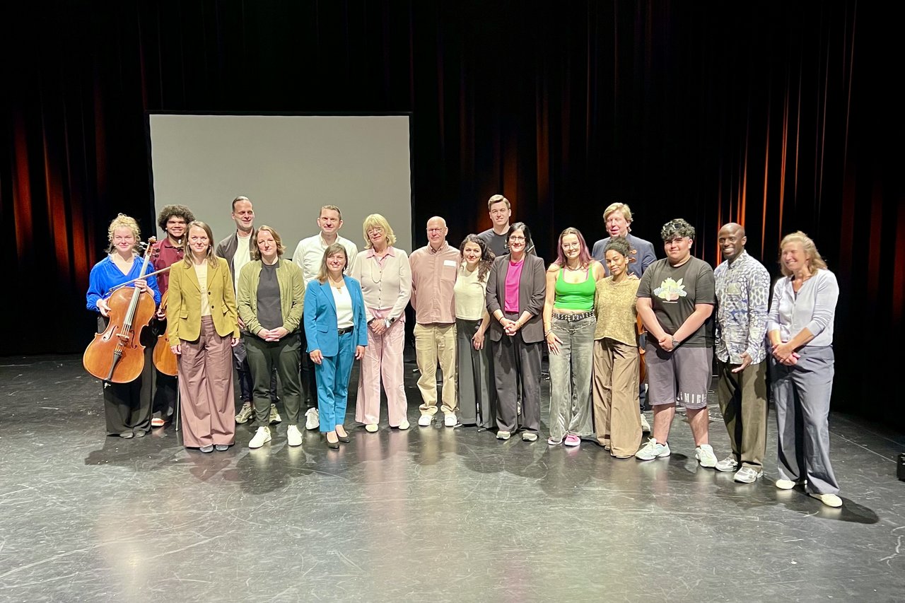 Viele Menschen stehen für ein Gruppenfoto auf einer Theaterbühne