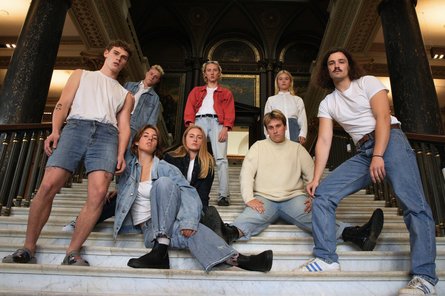 8 junge Menschen, von unten fotografiert stehen auf einer Marmortreppe.