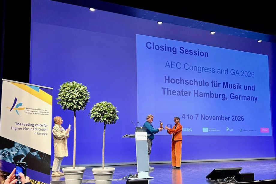 Drei Personen stehen auf einer Bühne und im Hintergrund ist eine Leinwand