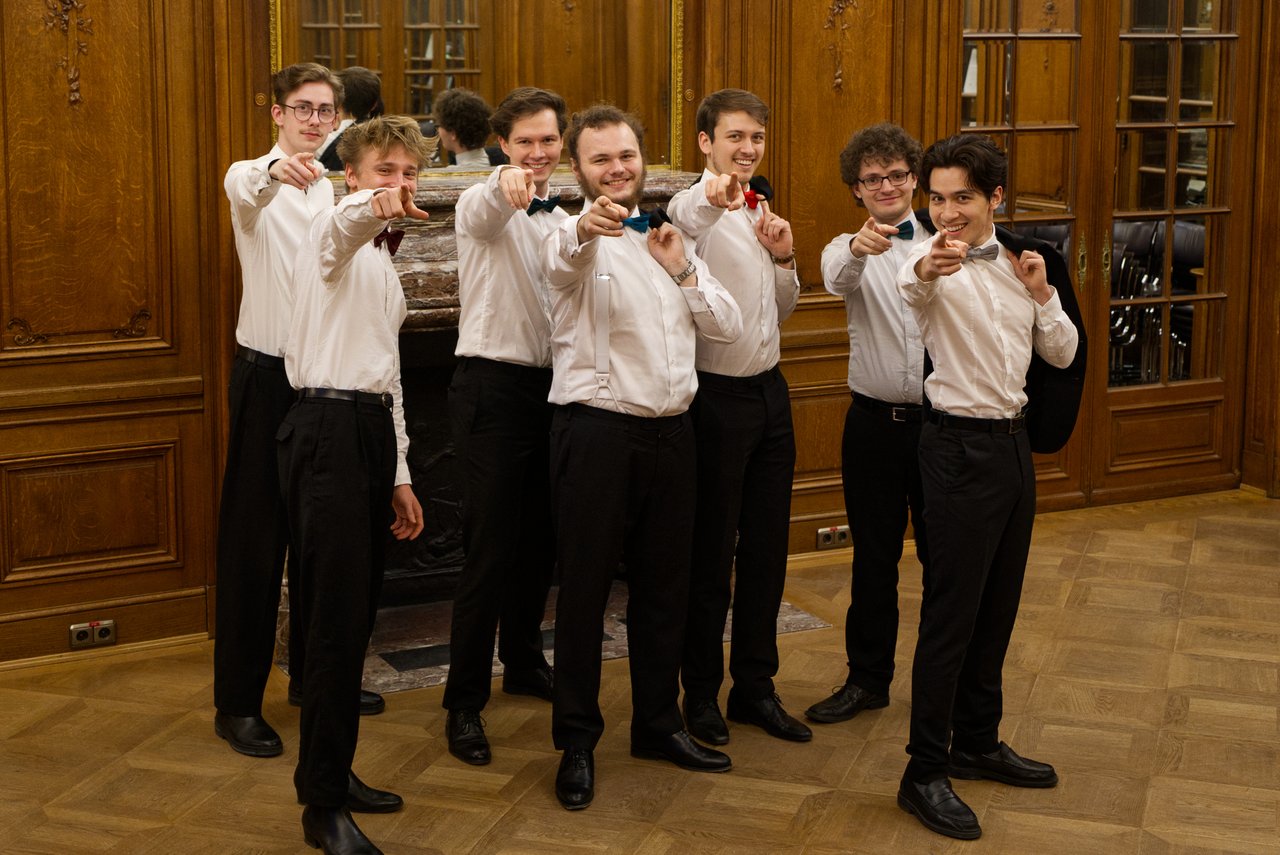der Männerchor steht frontal zur Kamera und zeigt darauf