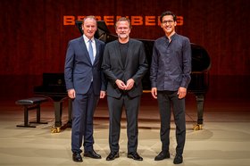 Drei Männer stehen auf einer Bühne vor einem schwarzen Flügel