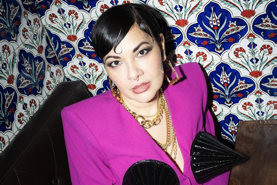 Lady Bitch Ray in pinkem Anzug mit Hörnern vor detailliert bemalten Fliesen