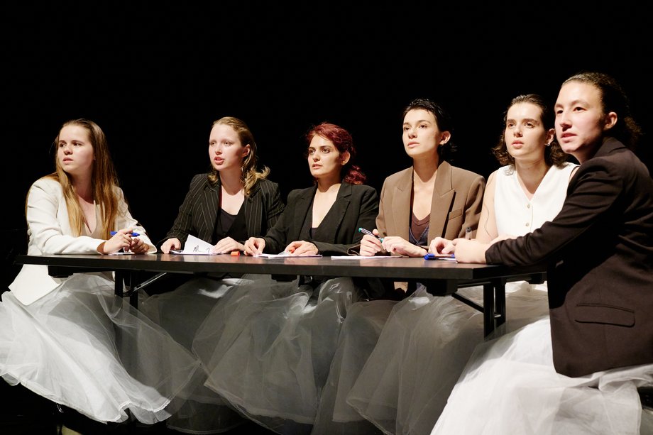 Actresses sit around a table and look into the audience