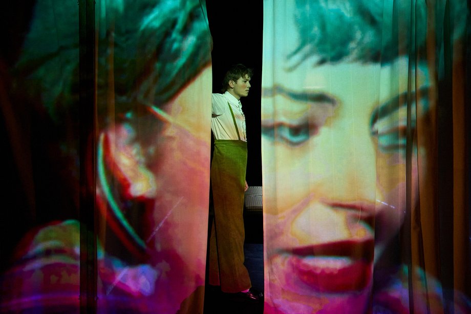 Stage curtain with large headshot. A man can be seen through a slit